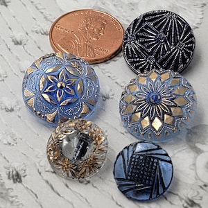 Op de afbeelding: Assortiment van zes vintage glazen knopen met blauwe en gouden ontwerpen. De knopen hebben verschillende patronen, waaronder bloemmotieven, geometrische en abstracte ontwerpen. De knopen zijn in uitstekende staat en zouden een geweldige aanvulling zijn op elk knutselproject.