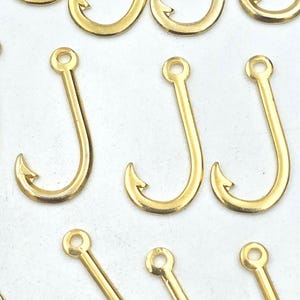 Puede incluir: Un conjunto de 12 abalorios de anzuelo de pesca de metal dorado. Los anzuelos miden aproximadamente 2,5 cm de largo y tienen un diseño sencillo.