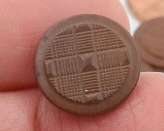 Puede incluir: Un botón de cerámica marrón con un patrón geométrico. El botón tiene un diseño en relieve con un patrón a cuadros.