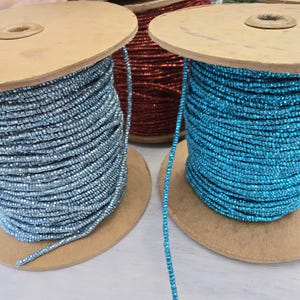 May include: Two spools of metallic thread, one blue and one red, are wound around cardboard spools. The spools are sitting on a white surface.