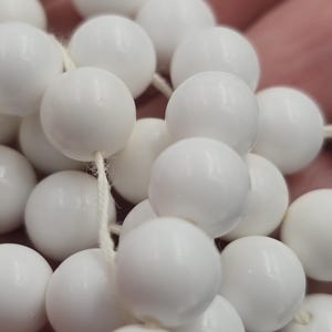 以下が含まれることがあります： 白い糸に白い丸いビーズが通されたもの。ビーズは滑らかで光沢があります。