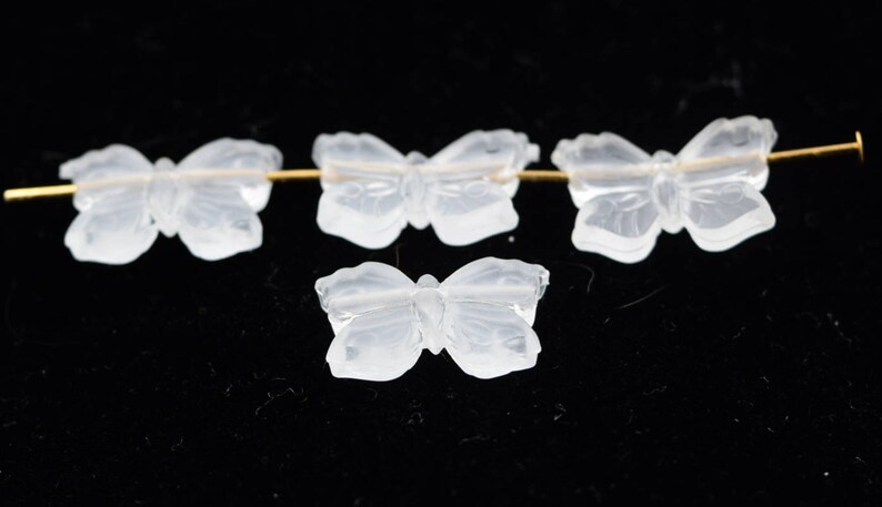 May include: Four clear glass butterfly beads strung on a gold wire. The beads are translucent and have a delicate, carved design.