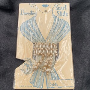 May include: A vintage package of pearl scarf slides, labeled "Decorative Scarf Slide" and "Made in Japan". The package features a drawing of a woman wearing a scarf and a close-up of the pearl slides.