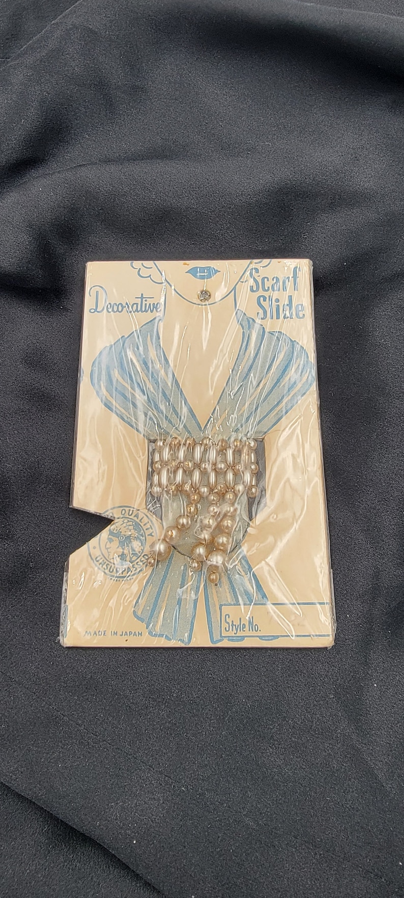 May include: A vintage package of pearl scarf slides, labeled "Decorative Scarf Slide" and "Made in Japan". The package features a drawing of a woman wearing a scarf and a close-up of the pearl slides.
