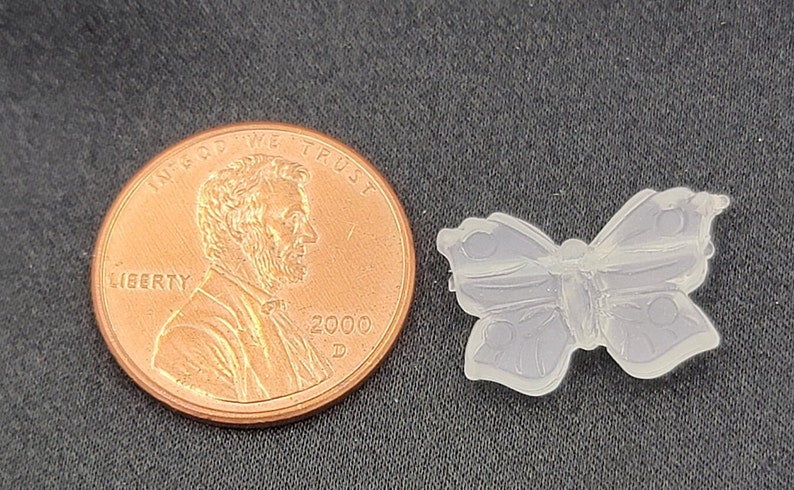 May include: A clear plastic butterfly charm, about the size of a UK penny. The butterfly has a detailed design with intricate wing patterns.