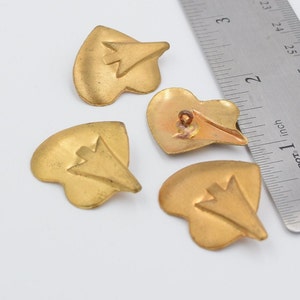 以下が含まれることがあります： 矢印のデザインが浮き彫りになった、金色のハート型のボタンが4つ。ボタンの直径は約2.5cmです。