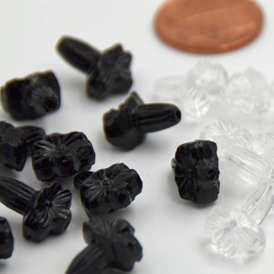 Puede incluir: Primer plano de dos tipos de botones de pl&aacute;stico con forma de flor. Los botones son negros y transparentes. Los botones negros tienen un dise&ntilde;o de flor en relieve y un peque&ntilde;o poste en la parte posterior. Los botones transparentes tienen una superficie lisa y un peque&ntilde;o poste en la parte posterior.