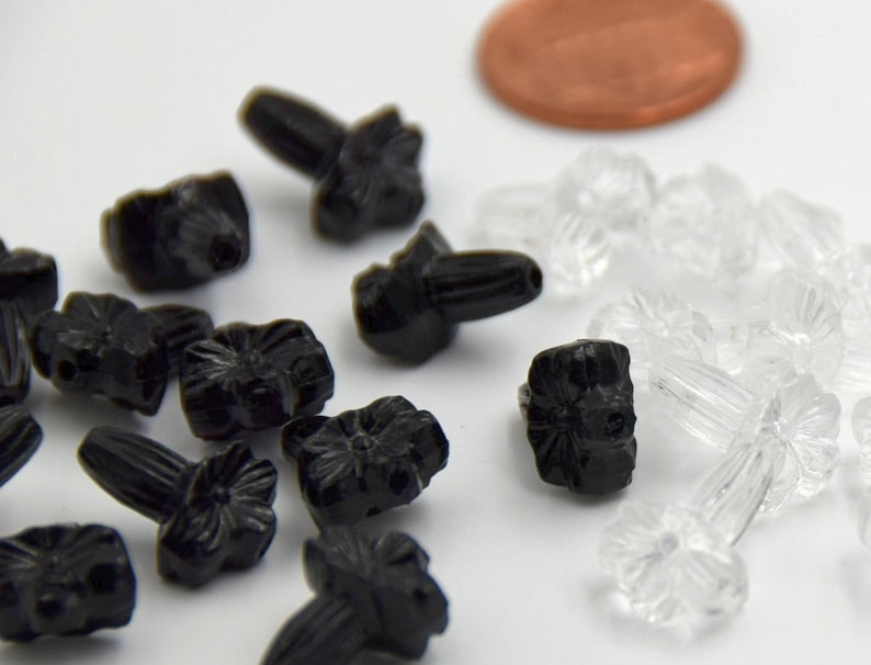 Puede incluir: Primer plano de dos tipos de botones de pl&aacute;stico con forma de flor. Los botones son negros y transparentes. Los botones negros tienen un dise&ntilde;o de flor en relieve y un peque&ntilde;o poste en la parte posterior. Los botones transparentes tienen una superficie lisa y un peque&ntilde;o poste en la parte posterior.