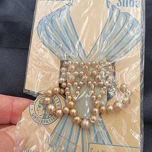 May include: A package containing a pearl necklace with a blue and white scarf printed with the text "Decorative Scarf Slide" and "Style No. 62". The package also has the text "Quality Unsurpassed" and "Made in Japan".
