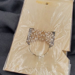May include: A close-up of a white pearl necklace packaged on a white card with a clear plastic cover.