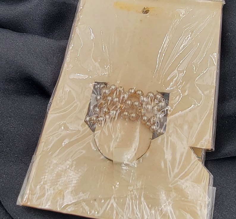 May include: A close-up of a white pearl necklace packaged on a white card with a clear plastic cover.