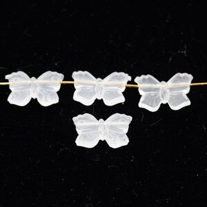 May include: Four clear glass butterfly beads, three of which are strung on a gold wire. The beads are translucent and have a delicate, intricate design.