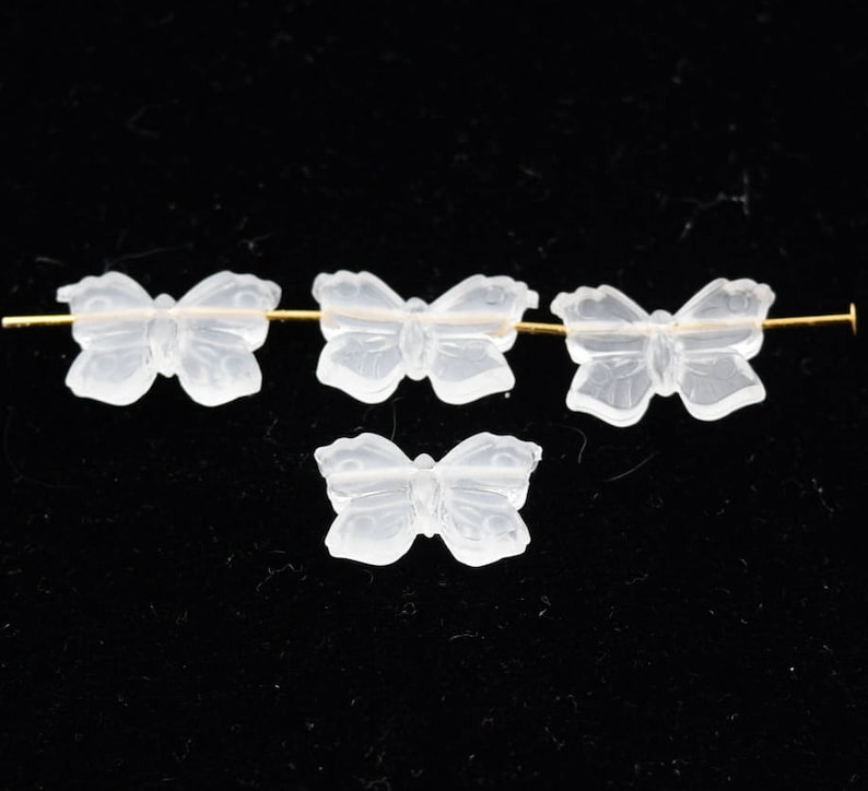 May include: Four clear glass butterfly beads, three of which are strung on a gold wire. The beads are translucent and have a delicate, intricate design.