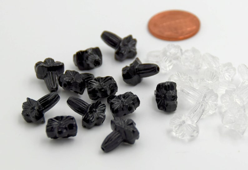 Puede incluir: Una colecci&oacute;n de cuentas de pl&aacute;stico en forma de flor, negras y transparentes. Las cuentas tienen un peque&ntilde;o tallo cil&iacute;ndrico. Hay 12 cuentas negras y 18 cuentas transparentes.
