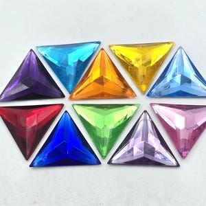 May include: Assortment of ten triangular shaped rhinestones in various colours, including red, orange, yellow, green, blue, purple, and clear.
