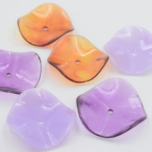 Puede incluir: Surtido de seis cuentas de plástico translúcido con forma de flor con un agujero en el centro. Dos cuentas son naranjas, dos son moradas y dos son moradas claras.