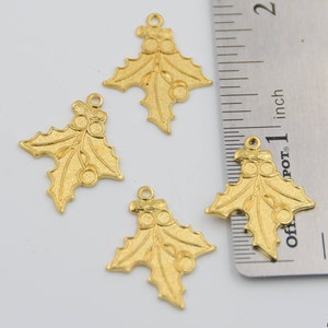 May include: Four gold-colored holly leaf charms with red berries. The charms are approximately 1 inch in size and have a loop at the top for hanging.