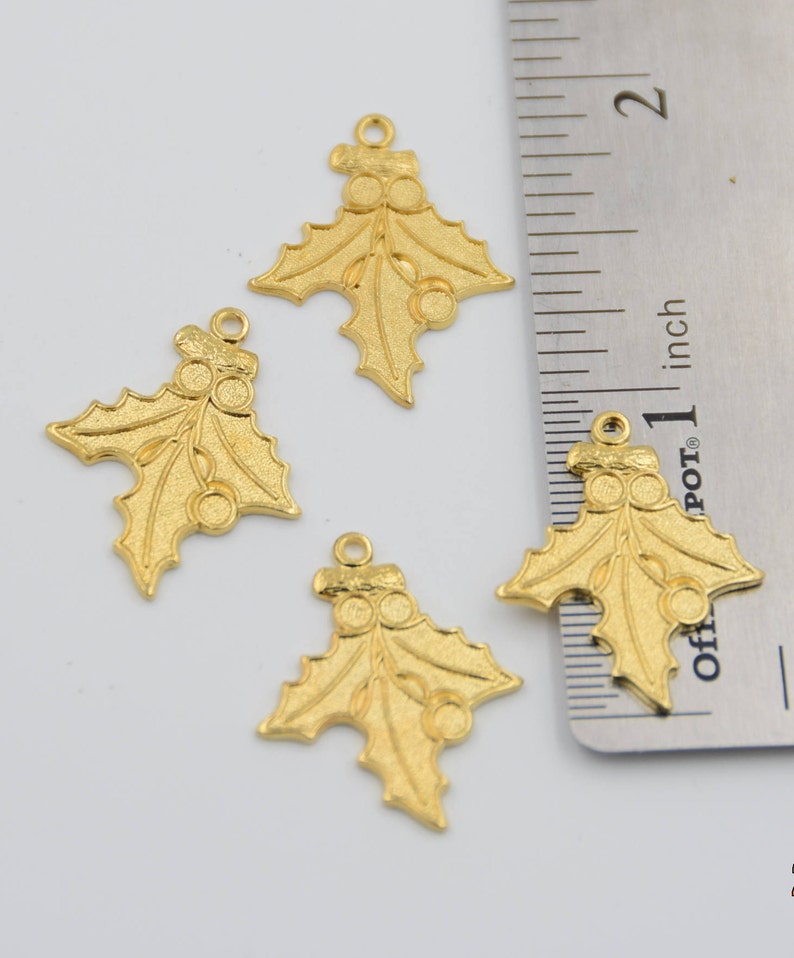 May include: Four gold-colored holly leaf charms with red berries. The charms are approximately 1 inch in size and have a loop at the top for hanging.