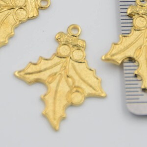 May include: Three gold-colored metal holly leaf charms with red berries. The charms are about 2 inches long and have a loop at the top for hanging.
