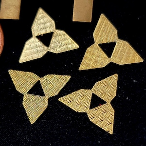 May include: Four gold-coloured metal triangular shapes with a smaller triangle cut out of the centre. The triangles have a textured surface.