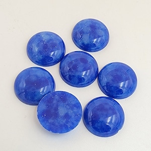 Puede incluir: Siete cabujones redondos azules con un acabado de purpurina blanca. Los cabujones tienen un diámetro de aproximadamente 2,5 cm.