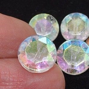 Könnte beinhalten: Vier schimmernde, klare Glasperlen mit facettiertem Design. Die Perlen haben einen Regenbogeneffekt.