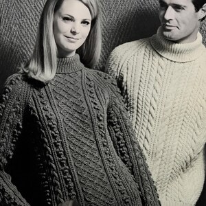 May include: A dark-colored long-sleeve sweater with a high turtleneck collar, featuring a complex knit pattern of vertical cables, diamond shapes, and bobbles. Beside it, a light-colored long-sleeve sweater with a high turtleneck and cable knit.