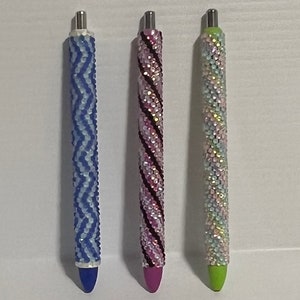 May include: Three pens with different colored sparkly designs. The pens are blue, pink, and green.