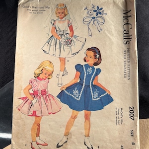Può includere: Modello di cucito vintage McCall's per un vestito e sottoveste per bambina, taglia 4. La copertina presenta illustrazioni di bambine con abiti, tra cui un vestito blu con ricami bianchi e un vestito rosa con un fiocco. Il modello include un transfer per due abiti.