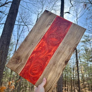 May include: A wooden cutting board with a red epoxy resin inlay. The resin has a swirling pattern and is a bright, vibrant red.