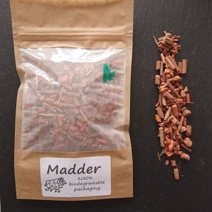 Puede incluir: Una bolsa de papel marr&oacute;n con una ventana transparente que contiene peque&ntilde;as virutas de madera de color marr&oacute;n rojizo etiquetadas como Madder. La etiqueta muestra una ilustraci&oacute;n de una oveja y el texto 100% biodegradable packaging. Un mont&oacute;n de virutas est&aacute; al lado.