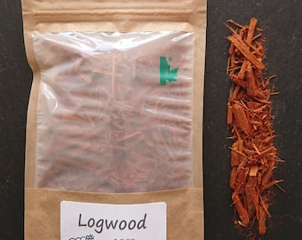 May include: A brown paper pouch with a clear plastic window containing reddish-brown logwood chips. A white label on the front reads Logwood, 100% biodegradable packaging, and features a small sheep illustration. Loose logwood chips sit nearby.