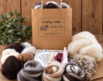 Puede incluir: Una bolsa de regalo de papel marrón con un asa de cinta de cuadros vichy morada, etiquetada como Crafty Jam Craft Kits con una ilustración de oveja. La bolsa está rodeada de ovillos de lana cardada en tonos blanco, marrón y gris.