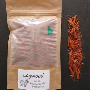 Puede incluir: Una bolsa de papel marr&oacute;n con una ventana de pl&aacute;stico transparente que contiene virutas de palo de campeche de color marr&oacute;n rojizo. Una etiqueta blanca dice Logwood, 100% biodegradable packaging, con un dibujo de una oveja. Virutas sueltas.