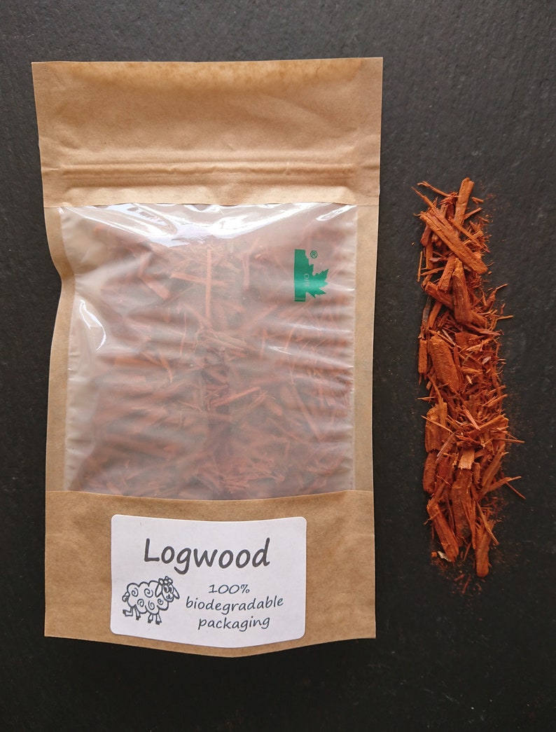 Puede incluir: Una bolsa de papel marr&oacute;n con una ventana de pl&aacute;stico transparente que contiene virutas de palo de campeche de color marr&oacute;n rojizo. Una etiqueta blanca dice Logwood, 100% biodegradable packaging, con un dibujo de una oveja. Virutas sueltas.