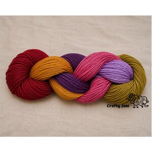 Puede incluir: Una madeja de hilo trenzada con una paleta de colores vibrantes que incluye rojo intenso, amarillo mostaza, morado oscuro, rosa fuerte, lavanda claro y verde oliva. El texto Crafty Jam est&aacute; impreso en negro en la esquina inferior derecha.