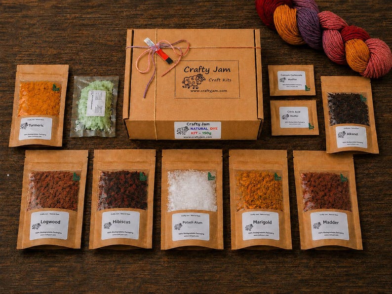 Puede incluir: Una caja de cart&oacute;n marr&oacute;n etiquetada como Crafty Jam Craft Kits con un kit de tinte natural, rodeada de varias bolsas peque&ntilde;as que contienen diversos polvos coloridos y materiales vegetales secos, adem&aacute;s de una madeja de lana multicolor.