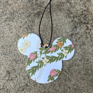 May include: A white car air freshener shaped like Mickey Mouse's head with a floral pattern. The air freshener has a black string for hanging.