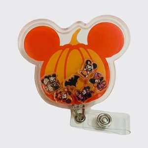 Pode incluir: Um porta-crachá de plástico transparente com tema de Halloween em forma de abóbora com orelhas do Mickey Mouse. A abóbora é laranja e amarela com uma variedade de pequenos personagens com tema de Halloween dentro.