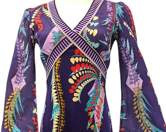 May include: A long-sleeved maxi dress with a V-neckline and a colorful floral print on a purple background. The dress has bell sleeves and a fitted bodice.
