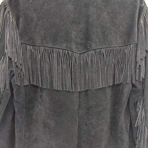 May include: Black suede jacket with fringe detailing across the back and sleeves. The jacket has a classic western style with a notched collar and a button-up front. The fringe is long and hangs down from the yoke and sleeves.