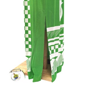 May include: A green garment with white geometric patterns, including checks and angled lines, is displayed. The fabric is draped over a wooden structure, showcasing the design's details. The garment's design is visible, with a split down the center.