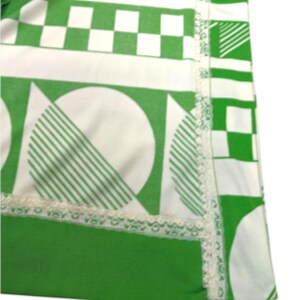 May include: A section of a green and white patterned textile. The design includes geometric shapes like squares, circles with striped segments, and lines. A white lace trim borders the edge of the fabric.