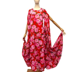 May include: A vintage red dress with a floral pattern of pink roses. The dress features a round neckline and flowing cape sleeves. The dress is displayed on a wooden mannequin.
