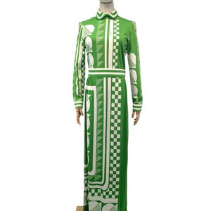May include: A long, green dress with a white geometric pattern. The dress features long sleeves, a collared neckline, and a fitted waist. The pattern includes squares, circles, and lines. The dress is displayed on a mannequin.