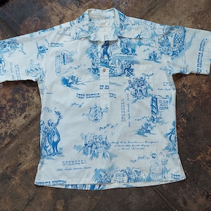 May include: A white short-sleeved button-down shirt with a blue and white pattern. The pattern features musical notes, a barbershop pole, and the text "Keep America Singing" and "SPEBSQSA Aloha Chapter Honolulu, Hawaii".