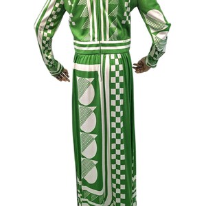 May include: A green and white patterned maxi dress. The dress features a high collar, long sleeves, and a full-length skirt. The design includes geometric shapes such as triangles, squares, and semi-circles. The dress is made of a knit fabric.