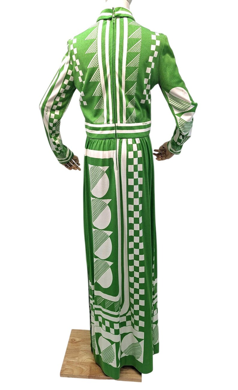 May include: A green and white patterned maxi dress. The dress features a high collar, long sleeves, and a full-length skirt. The design includes geometric shapes such as triangles, squares, and semi-circles. The dress is made of a knit fabric.