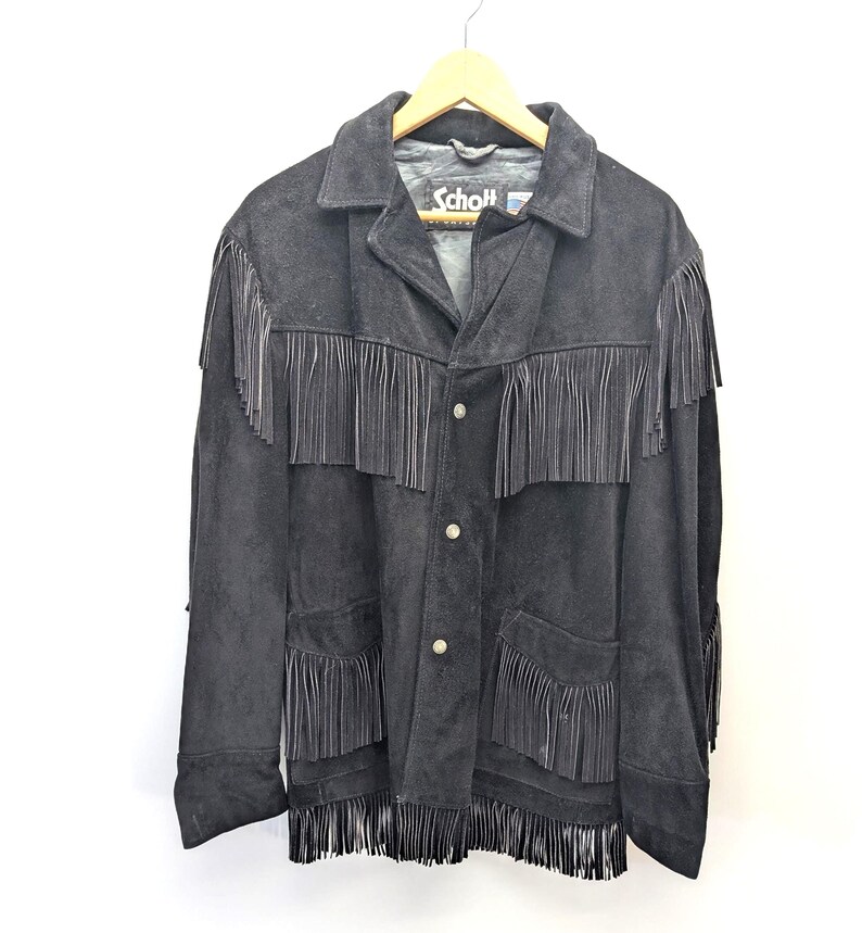 May include: Black suede jacket with fringe detailing. The jacket has a collared neckline, button-up front, and pockets. The brand name "Schott" is visible on the label. The fringe is along the sleeves, pockets, and the bottom hem.