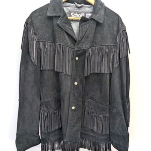 May include: Black suede jacket with fringe detailing. The jacket has a classic collar, button closure, and two front pockets. The brand name "Schott" is visible on the label. The fringe is along the chest, pockets, and sleeves.